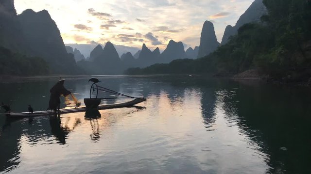 The traditional Chinese cormorant fisherman casting his net into the beautiful Li river in Yangshuo - Guilin . These days however only a few cormorant fisherman remain.