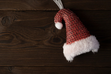 Obraz na płótnie Canvas Red Santa hat with white fur and small red gift bag for gifts on natural brown wooden background.