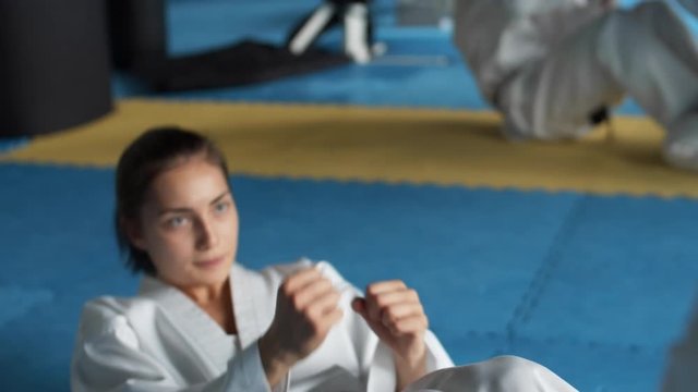 Close up of young female karateka wearing kimono doing abdominal crunches in fighting center while her teammates exercising on background