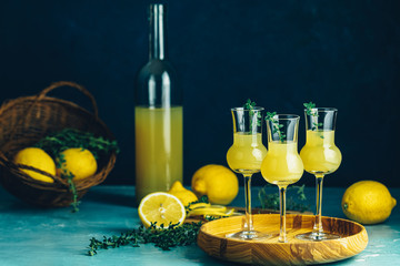 Limoncello with thyme in three grappas wineglass in wooden tray, fresh lemon in basket. Artistic...
