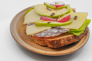 Sandwich complet avec de l'avocat et des rondelles de radis sur des tranches de fromages de brebis et de la charcuterie sur une tranche de pain aux céréales assiete en céramique de Vallauris France