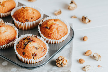 Vanilla caramel muffins in paper cups on white wooden background. Delicious cupcake with raisins, almonds and nuts. Homemade biscuit cakes. Copy space for text.