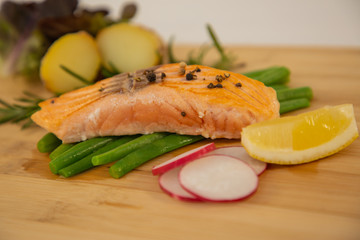 Grilled fresh salmon steak with roasted green beans, baked potatoes, lime and salad vegetables is a healthy diet for dieting on a wooden plate.