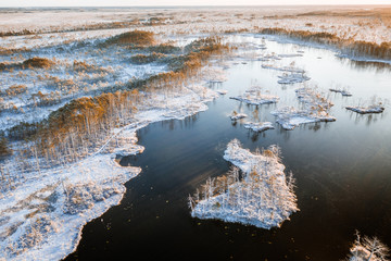Aerial view on National park covered in first snow in Latvia. Warm sunlight lights up the frozen lake and islands.