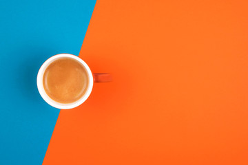 Fresh brewed coffee in ceramic cup over orange and blue background. Place for text.