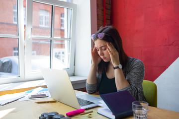 Tired female  marketer having headache during her work day in company , sitting at table with open laptop computer