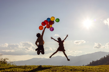 Two children jumping playing with colored balloons at sunset.