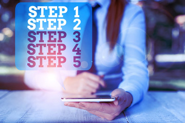 Writing note showing Step 1, 2, 3, 4 and 5. Business concept for Steps levels of a process work flow Female business person sitting by table and holding mobile phone