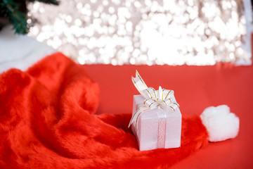 Christmas white gift box with a large bow standing on red hat santa calus against a background bokeh of twinkling golden bokeh lights. New Year's gift. Copy space