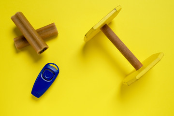 Two sticks of dog delicacy, clicker and wooden dumbbell, special training appliance, on bright yellow background.