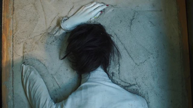 A mannequin resembling a human corpse lies face down in concrete.