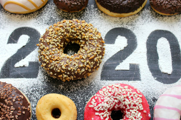 Text 2020 surrounded by colorful donuts on a black background vintage, new year concept. New year, Christmas background, copy space, figures 2020.