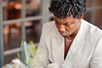 Stylish afro man in beige old school suit sitting on cafe with mobile phone. Fashionable young African male in casual jacket on bare torso.