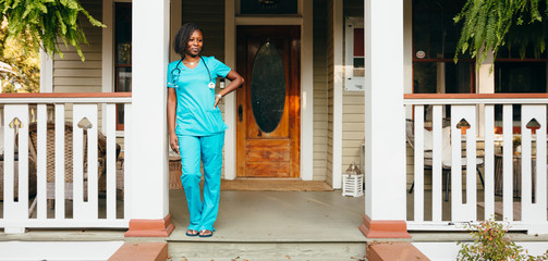 Healthcare professional leaning against pillar in front of house
