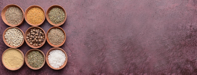 Bowls with different dry herbs and spices on color background