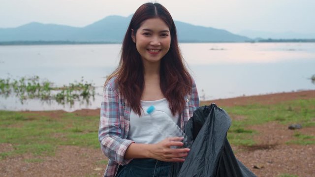 Portrait of young Asia lady volunteers help to keep nature clean up holding plastic bottle waste and black garbage bags on the beach. Concept about environmental conservation pollution problems.