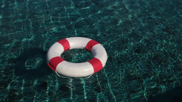 Lifebuoy Floating. Red life buoy over clear blue sea or ocean water background, swimming pool. Floating rescue buoy on the water surface. A floating lifebuoy. danger, 4 K slow-mo