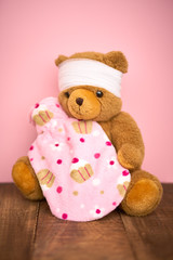 Bär Kuscheltier krank mit Verband und Wärmeflasche freigestellt auf pink Hintergrund