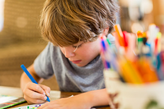 6 year old boy drawing amoung colorful pens