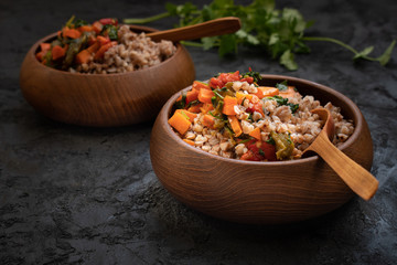 Vegan buckwheat groats cooked with carrot and roasted bellpepper served in wooden bowls - obrazy, fototapety, plakaty
