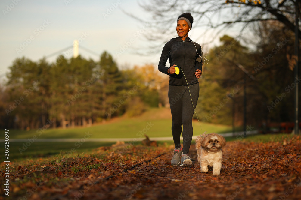 Wall mural happy black athletic woman running with a dog at the park.