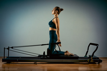 Young girl doing pilates exercises with a reformer bed. Beautiful slim fitness trainer on reformer...