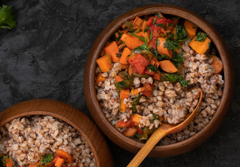 Vegan buckwheat groats cooked with carrot and roasted bellpepper served in wooden bowls