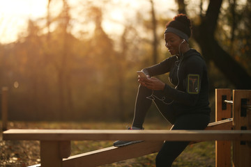 Happy black athletic woman text messaging on mobile phone in the park.