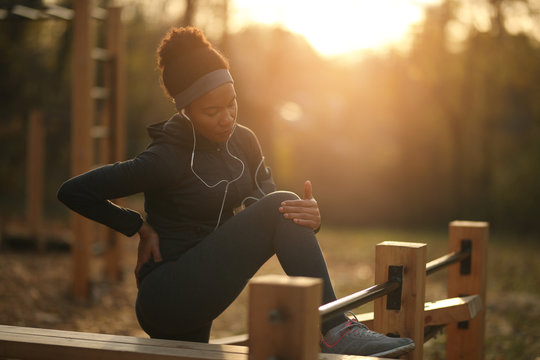 African American Athletic Woman Feeling Pain In Knee While Exercising At Sunset.