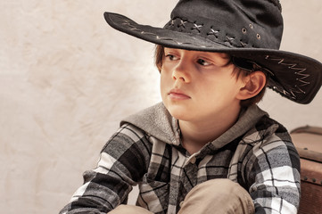 Fototapeta premium Boy model in a cowboy hat and a plaid shirt of blond with long hair in retro style. Vintage style