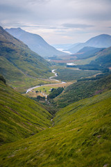 Panoramatic view on Scotland highland valley, during sunset with clouds, green yellow grass painting typical summer view with river in the middle