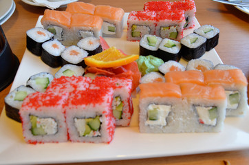 Salmon and caviar rolls served on a plate. sushi or rolls are held with chopsticks. with soy sauce, ginger and wasabi