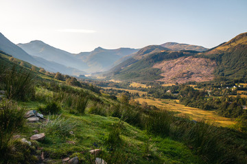 Naklejka premium Panoramatic view on Scotland highland valley, during sunset with clouds, green yellow grass painting typical summer view with river in the middle