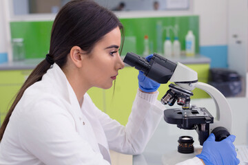 Young female scientist looking through a microscope in a laboratory doing research, microbiological analysis, medicine.