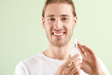 Handsome young man with cosmetic product on light background