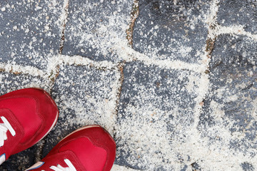 De-icing chemicals on the pavement.  Top view of red sneakers on asphalt sprinkled with technical...