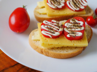 Sandwich with white bread, cheese, tomato on a plate and small baby tomatoes. Tea cup and napkin with spoon. Close up.