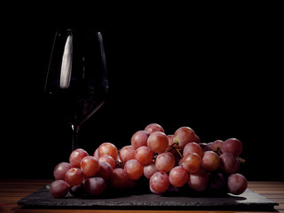 Glass of red wine and cluster of red fresh organic grapes on a black slate plate and wooden table....