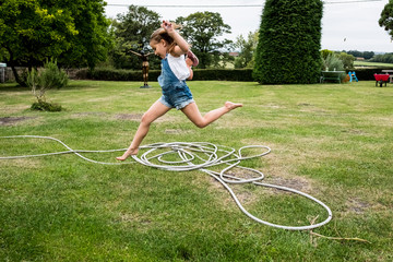 Girl jumping over hose in lawn