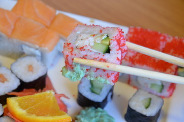 Salmon and caviar rolls served on a plate. sushi or rolls are held with chopsticks. with soy sauce, ginger and wasabi