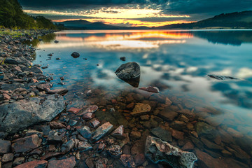Beatiful sunset over the dam in Scotland highland, with rocks in foreground, long exposure, blurred water