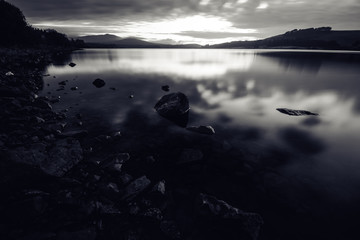 Beatiful sunset over the dam in Scotland highland, with rocks in foreground, long exposure, blurred water