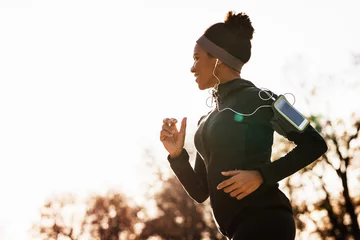 Poster Happy black sportswoman jogging while exercising in nature. © Drazen
