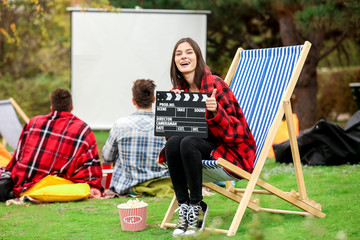 Happy young woman with movie clapper in outdoor cinema