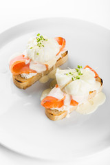 Bruschetta with salmon and poached egg on a white plate. Decorated with micro greens.