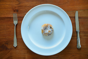 A large white plate from above on a wooden table top with knife and fork and a small piece of pastry on the plate