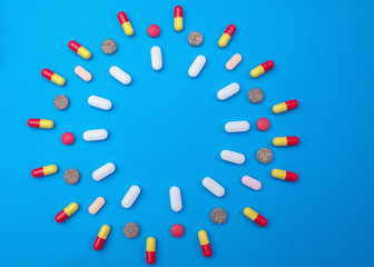 Group of different pills arranged in shape of circle on blue background