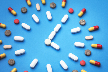 Group of different pills arranged in form of clock on blue background. Time in pharmacy. Time in medicine. 