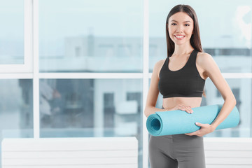 Fototapeta na wymiar Sporty young woman with yoga mat in gym