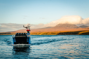 Drifting blue ferry ship between isle of Jura, in the background, and Isle of Skye, in Scotland at sunset time